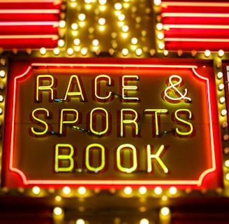 Bright neon lights on a marquee sign display the words 'RACE & SPORTS BOOK'. The sign is surrounded by rows of yellow and white lights against a red background, evoking a vibrant, energetic atmosphere typically associated with casinos or entertainment venues.